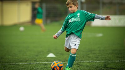 En kille i grön tröja sparkar på en fotboll.