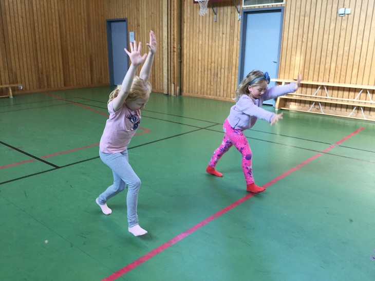 Saga och Melina står i en gymnastiksal. De har båda händerna i luften och är påväg att göra en kullerbytta.