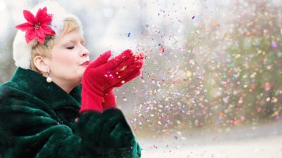 En kvinna med grön jacka och röda handskar blåser glitter från sina händer
