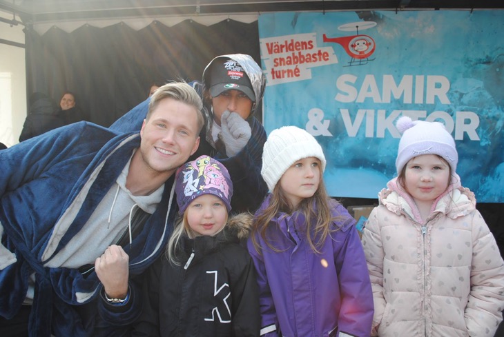 Artisterna Samir och Viktor ler mot kameran tillsammans med tre barn framför en plansch det står Samir & Viktor på.