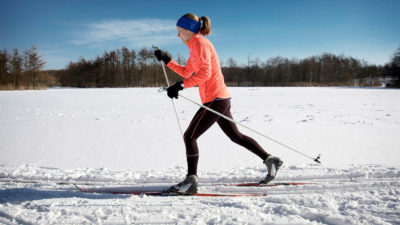 Motionsklädd skidåkare glider fram genom snö under klarblå himmel.