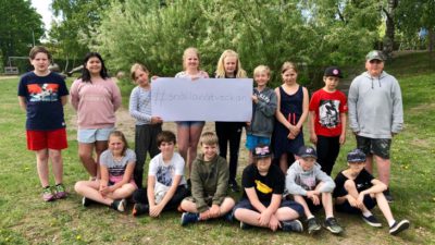 15 skolbarn på en gräsmatta håller i en skylt med texten #snällanätveckan.
