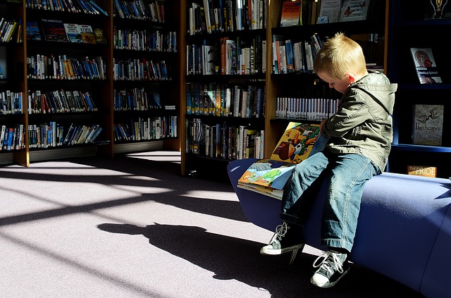 Ett barn sitter på ett bibliotek och bläddrar i en bok.