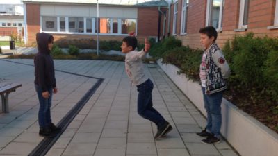 Tre barn leker intill skolbyggnad.