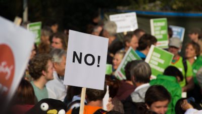 Flera politiska budskap syns på skyltar i en stor folkmassa. På skylten längst fram står det "NO!" som i "Nej!".