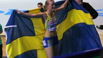 Moa Hjelmer har fått en stor svensk flagga efter ett lopp. Hon håller upp den som en mantel inför publiken.