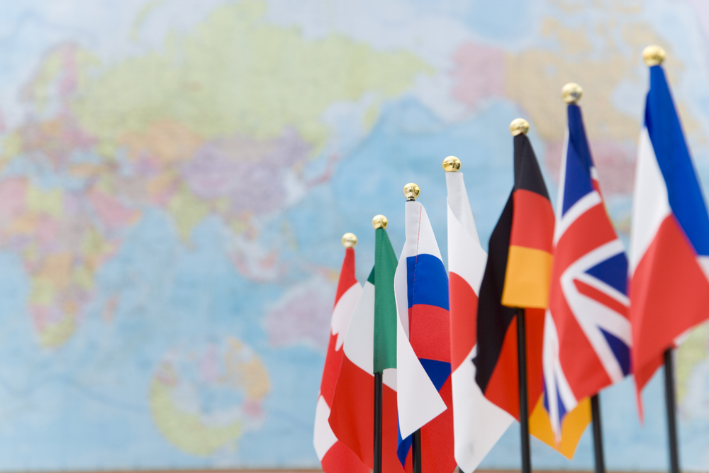 G7-ländernas falggor hänger i rad. Bakom dem syns en världskarta.