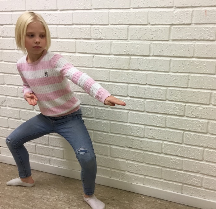 Ung tjej visar ett karateslag framför en vit tegelvägg.