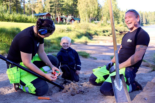 Elin, Dylan och Nicke sitter i sanden med spadar och ska precis öppna paketet.
