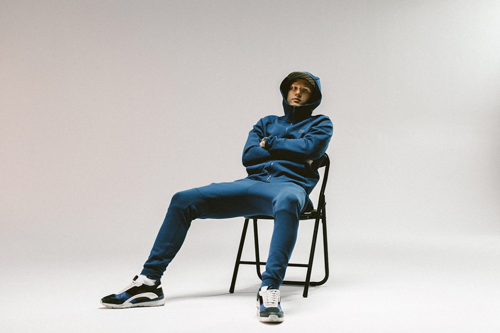 Rapparen Einár sitter i en stol. Han har en jacka med luvan uppdragen.